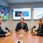 Réunion professionnelle de trois dirigeants dans une rédaction sportive, autour d’une table, avec des écrans présentant des images de football, d’entraînement de MMA et des graphiques abstraits d’abonnements.